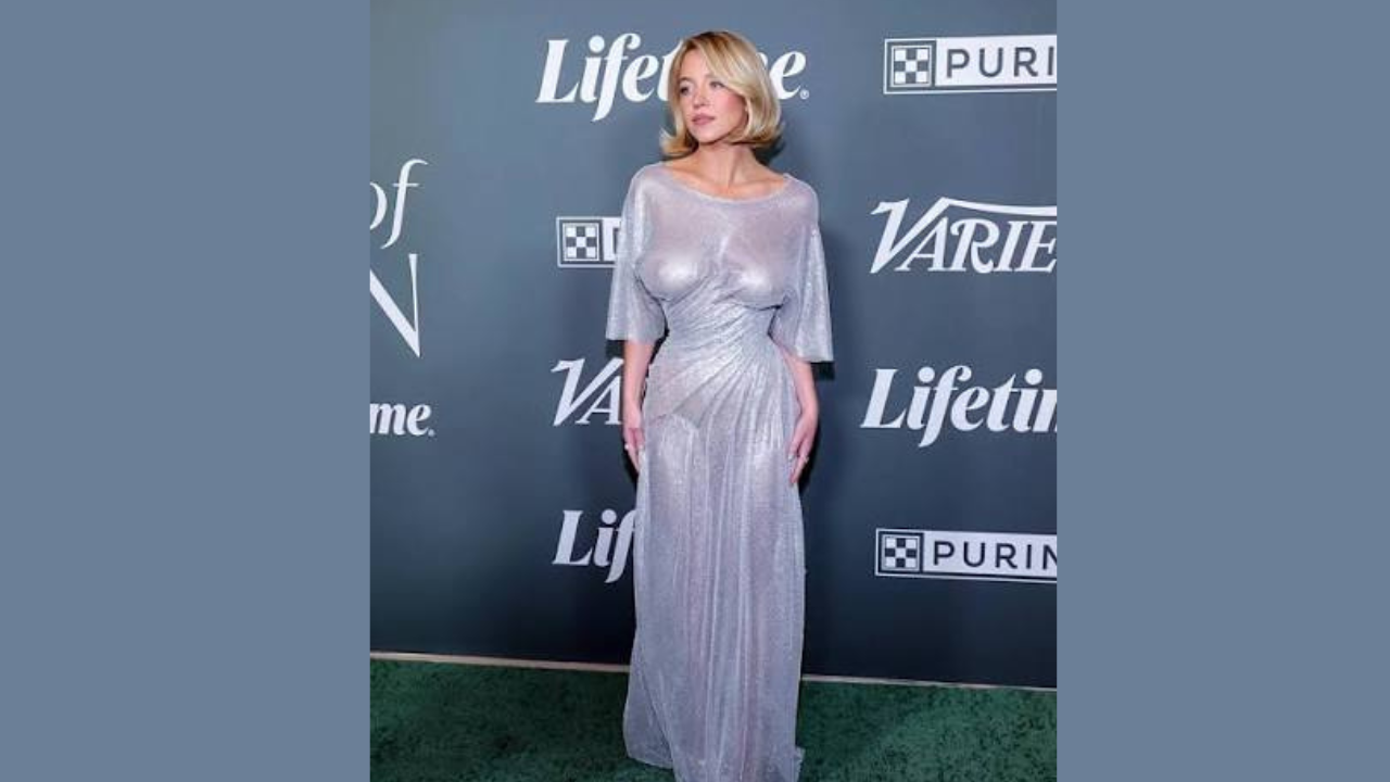 Sydney Sweeney wearing a silver dress stands elegantly on a lush green carpet, showcasing her style.