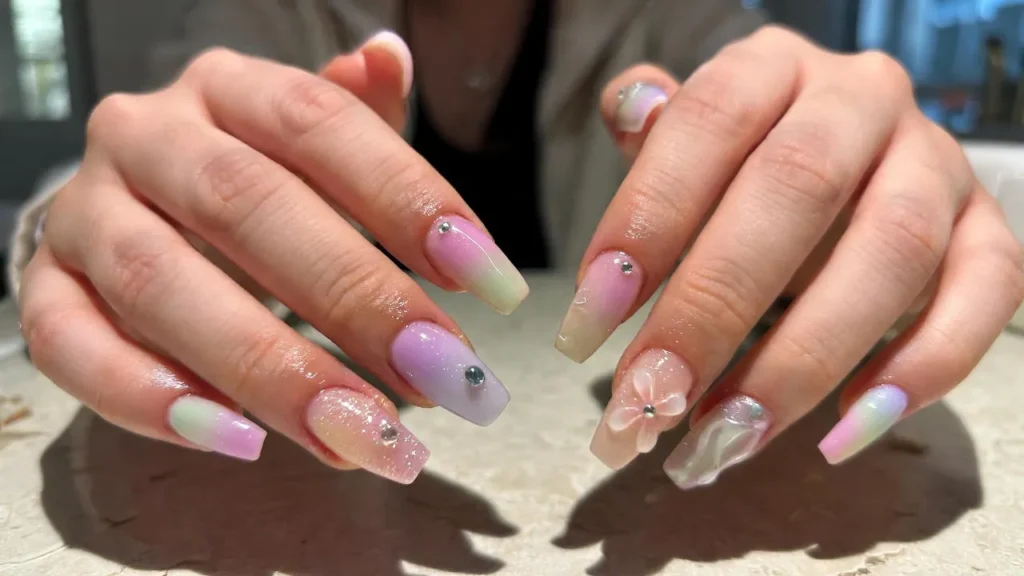 Hands showing long glossy Gel X Nails in pastel colors with subtle glitter and nail art.