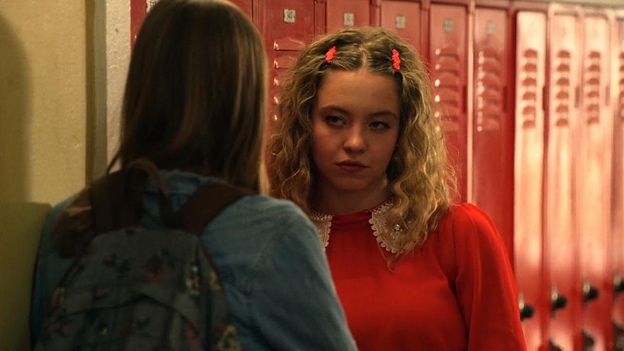 Sydney Sweeney in a red dress engages in conversation with another woman, both smiling and appearing friendly.